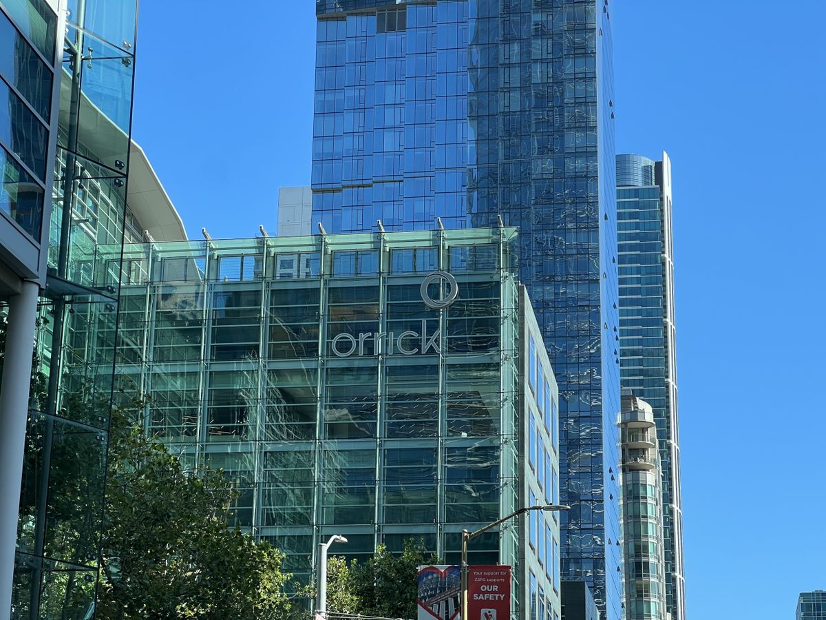 Low-angle view of the glass and steel Orrick Building, on a sunny day, with more glass-box skyscrapers in the background in San Francisco, California