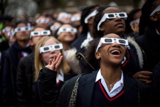 Students in the United Kingdom observe a partial solar eclipse while wearing protective solar-viewing glasses.