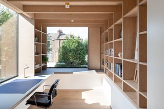 A study with wall to wall desks, wooden wall storage, wooden floors and large windows.