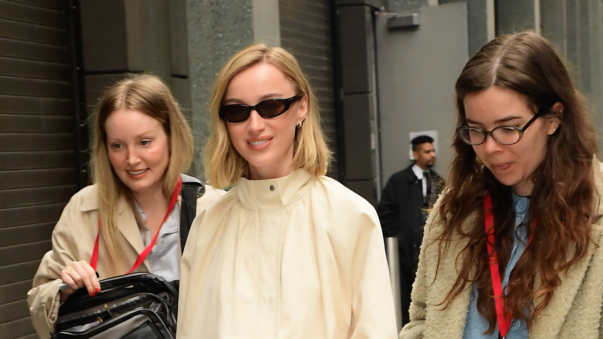 Phoebe Dynevor wearing a cream funnel neck jacket, a matching skirt, and black flats.