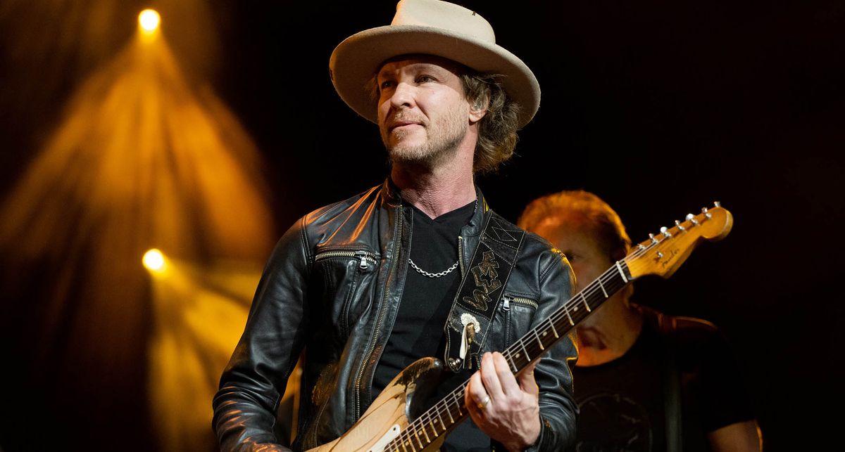 Kenny Wayne Shepherd wears a black leather jacket and a khaki wide-brimmed hat onstage as he plays a worn-in Fender Stratocaster.