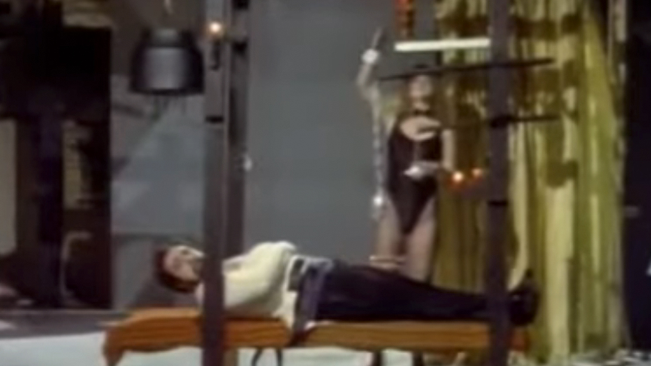 A magician in a straight jacket, lying on a bench with a weight above his head in Faces of Death