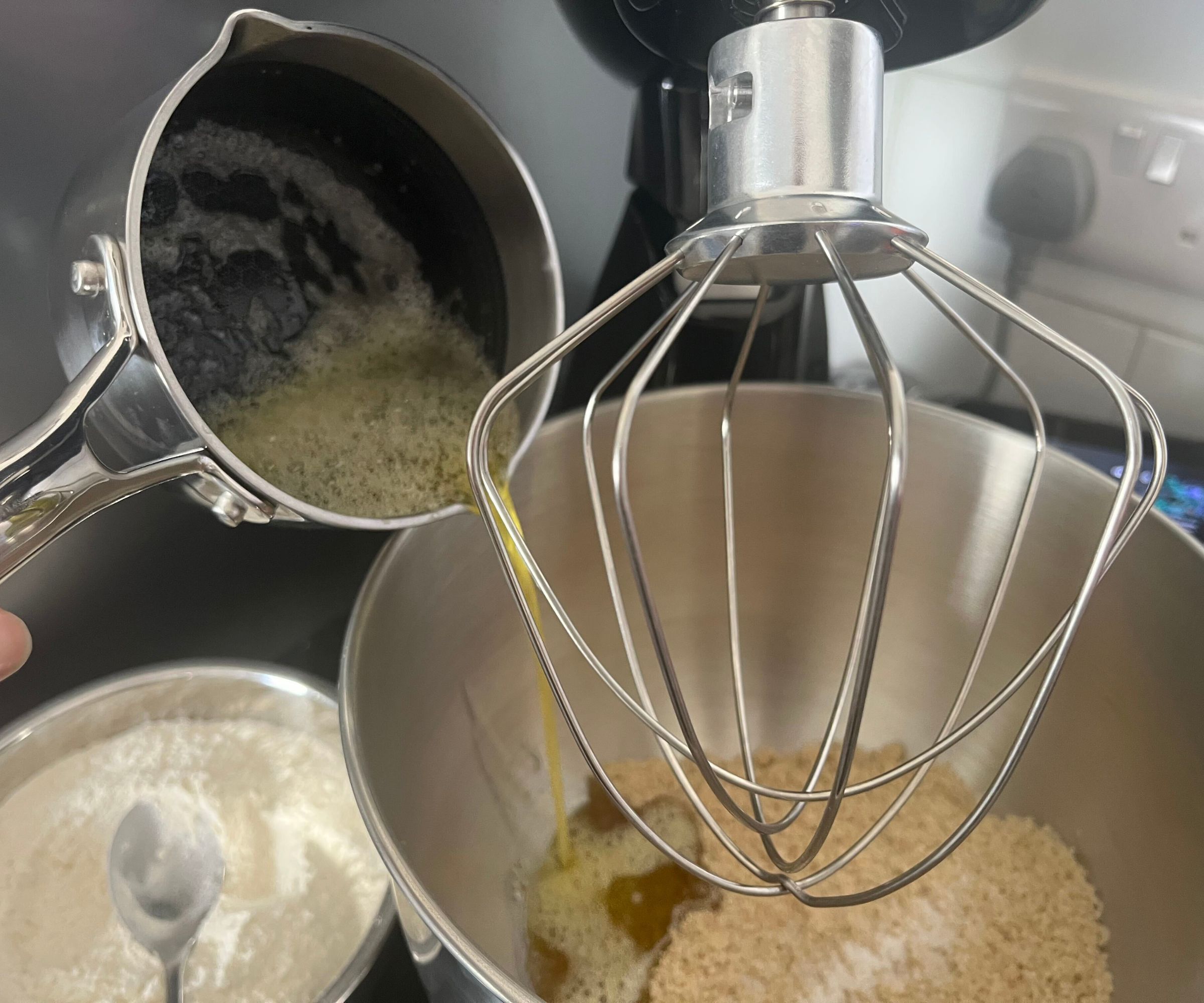 Pouring melted butter into the stainless steel bowl of the SMEG Forte Stand Mixer, fitted with a wire wisk. 