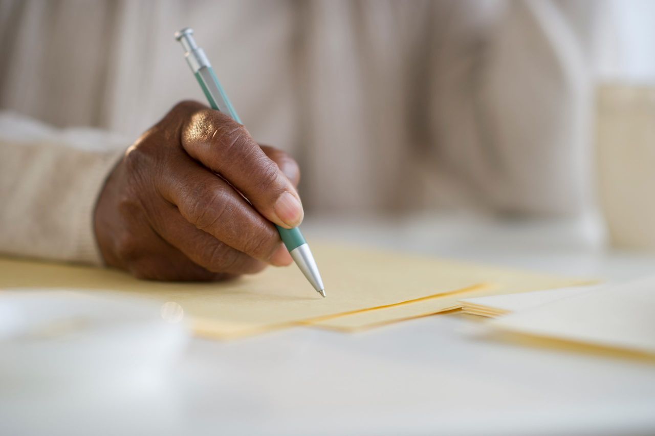 A woman&#039;s hand holding a pen and preparing to write on some yellow card