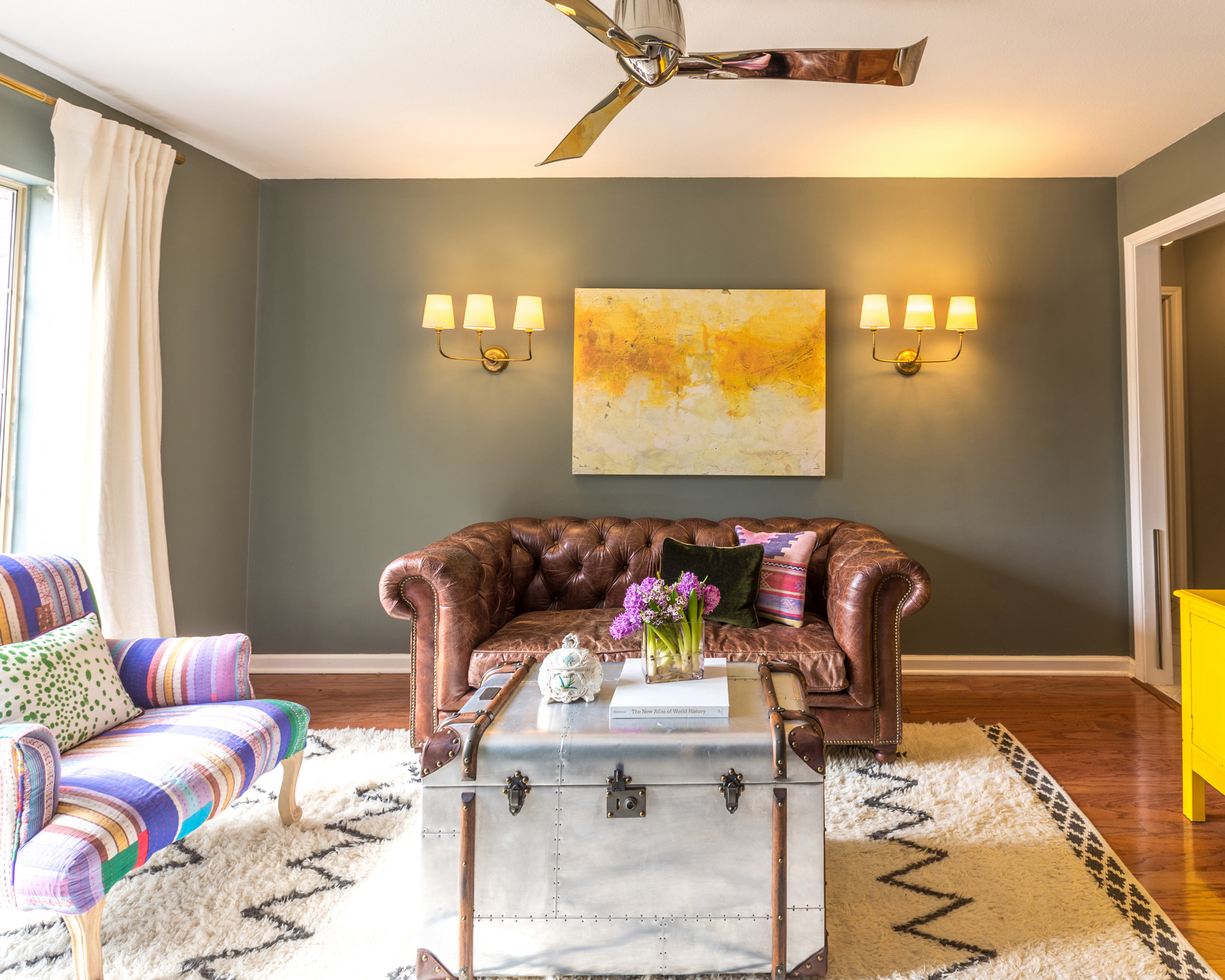 Lounge with leather sofa, multi colored sofa, yellow sideboard, chalky green walls, and alternative trunk coffee table.