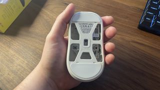 A Pulsar X2 CrazyLight gaming mouse in-hand, upside down, showing the holes in its underside.