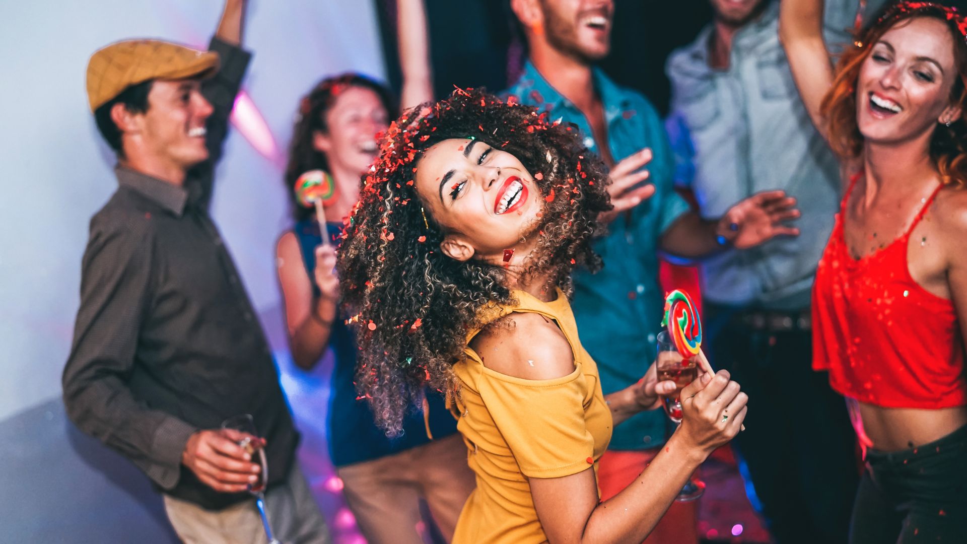 Happy friends doing party at night club - Young woman having fun with her group of mates eating candy lollipops inside disco - People, friendship, nightlife and youth holidays lifestyle