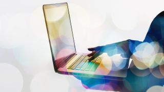 Somebody holding a laptop while standing with abstract colours surrounding them