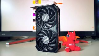 MSI RTX 4060 graphics card standing vertical on white desk with red dragon mascot toy on right