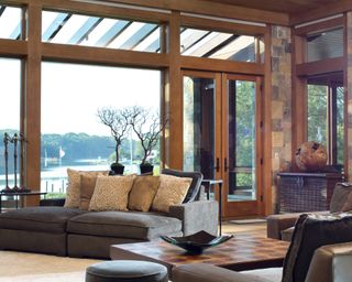A living room with floor to ceiling glass windows with warm wood beams
