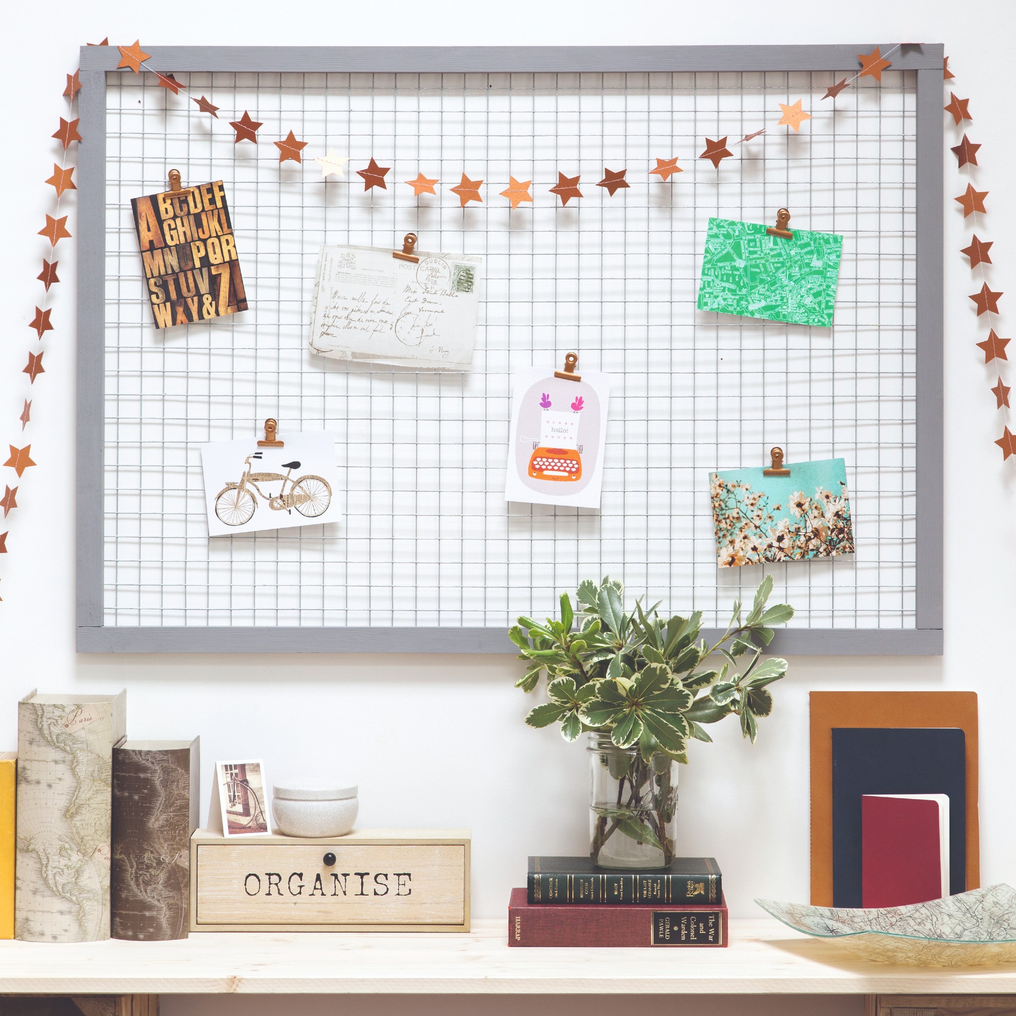 A metal wire notice board displaying greeting cards and postcards hung above a console table displaying decorative items