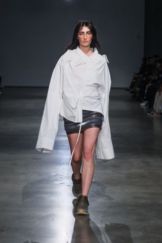 A model in a white button-down wrap shirt and mini skirt in Jane Wade Fall 2024 runway show.