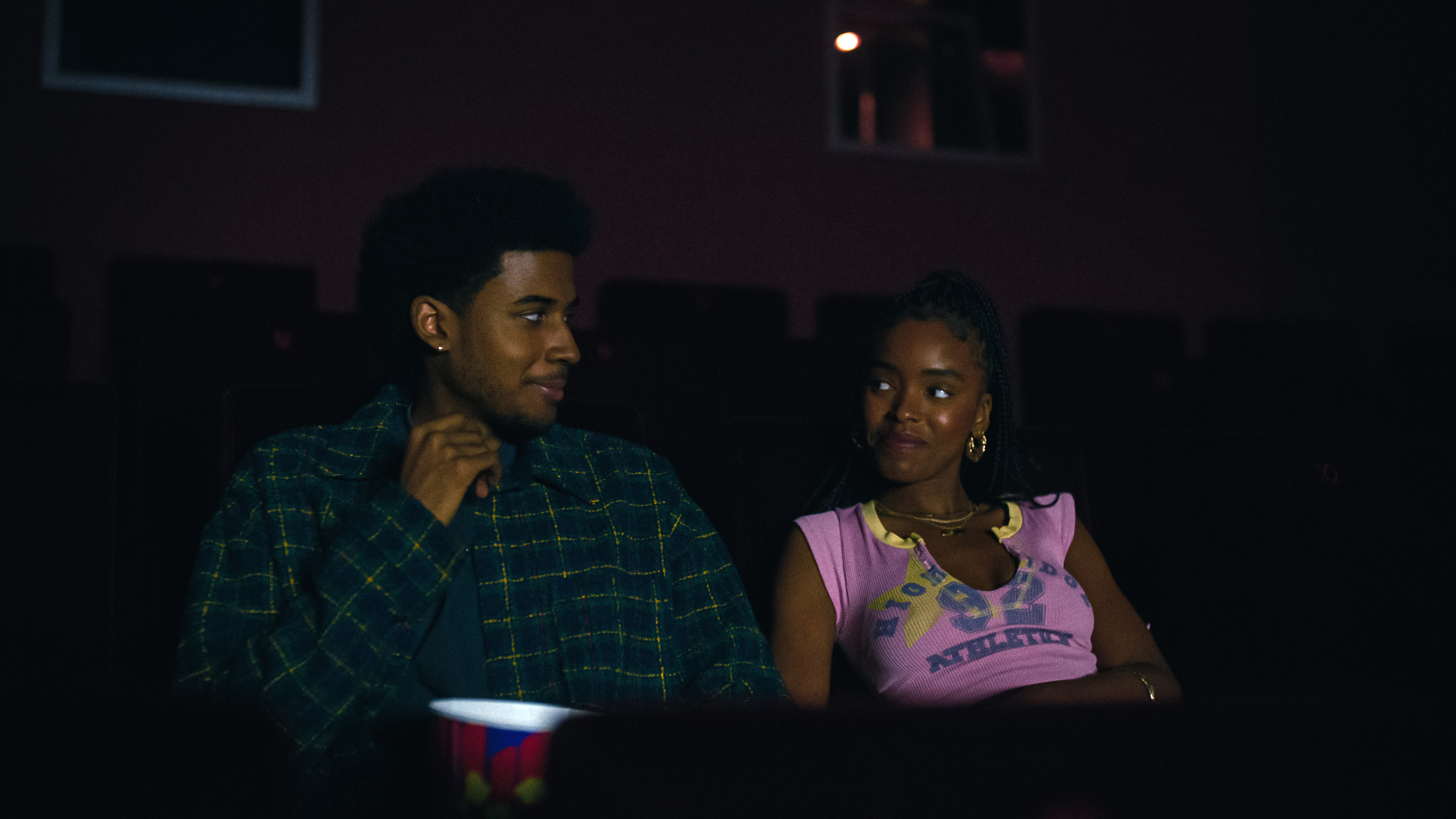 Michael Cooper Jr. as Justin Edwards and Lovie Simone as Keisha Clark smiling at each other in a movie theater in Forever on Netflix 