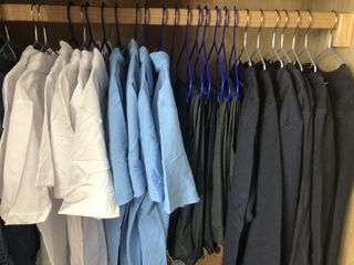 White and blue shirts hang alongside grey school trousers in a wardrobe.