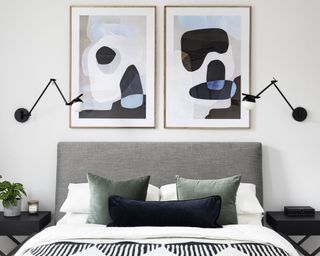 Bedroom with symmetrical double bed design, artwork above bed, matching black wall lights, gray headboard, white and black bedding, gray cushions, black wooden side tables