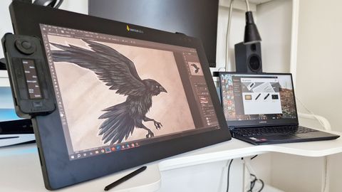 A photo of the Xencelabs Pen Display 24 tablet on a desk next to a laptop with a painting of a raven on the screen