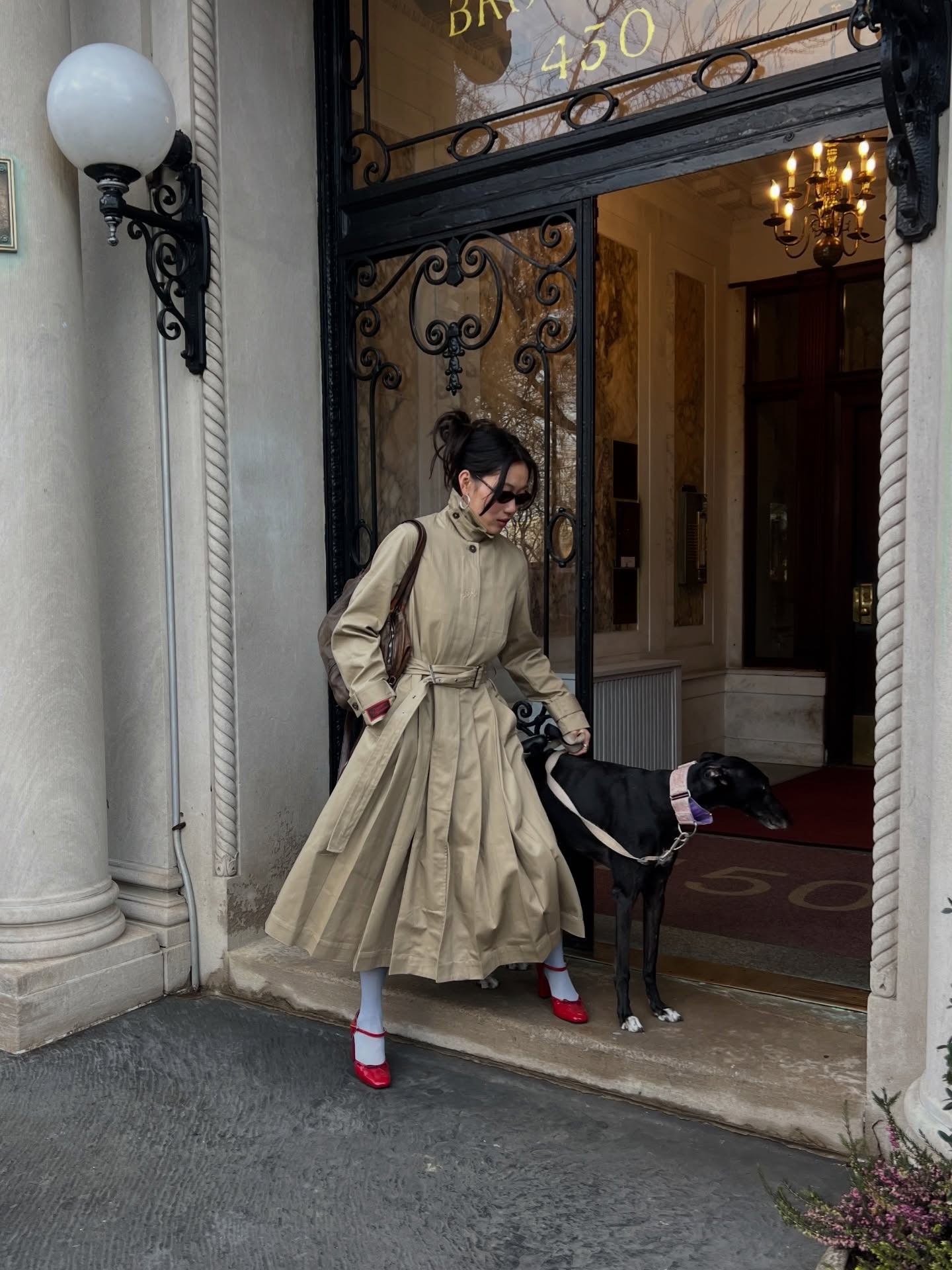 Woman wears full length funnel-neck trench coat with blue tights and red shoes