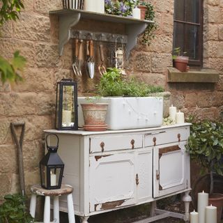 garden with vintage sideboard and sink, lanterns, shelf with hooks, tools hanging from it, pots, plants, candles