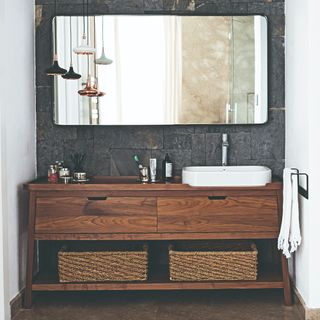 A bathroom with a large mirror and a dark wood under-sink cabinet with storage baskets