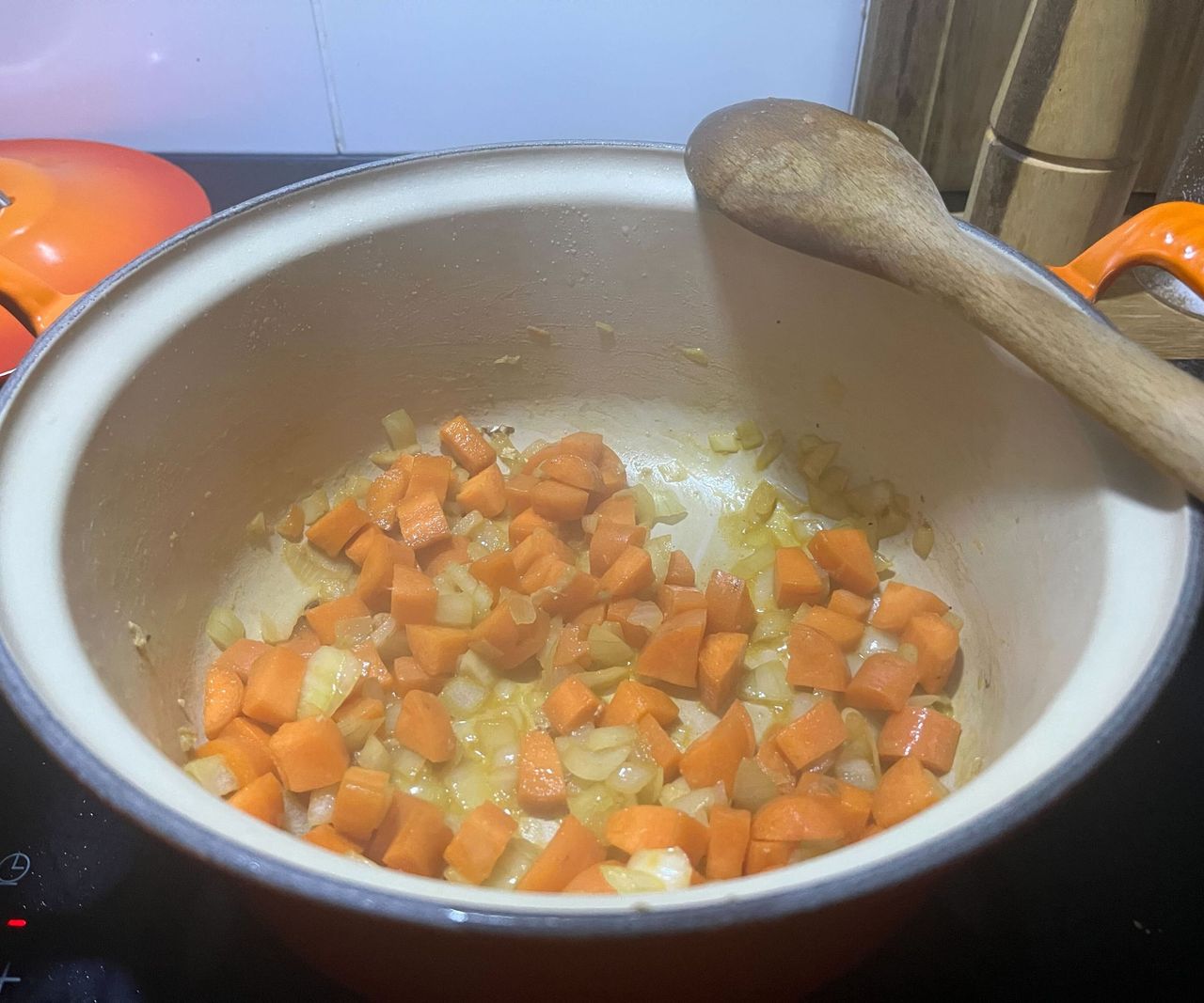 Saut&eacute;ing carrots and onions in a Dutch oven, with a wooden spoon balancing on the rim