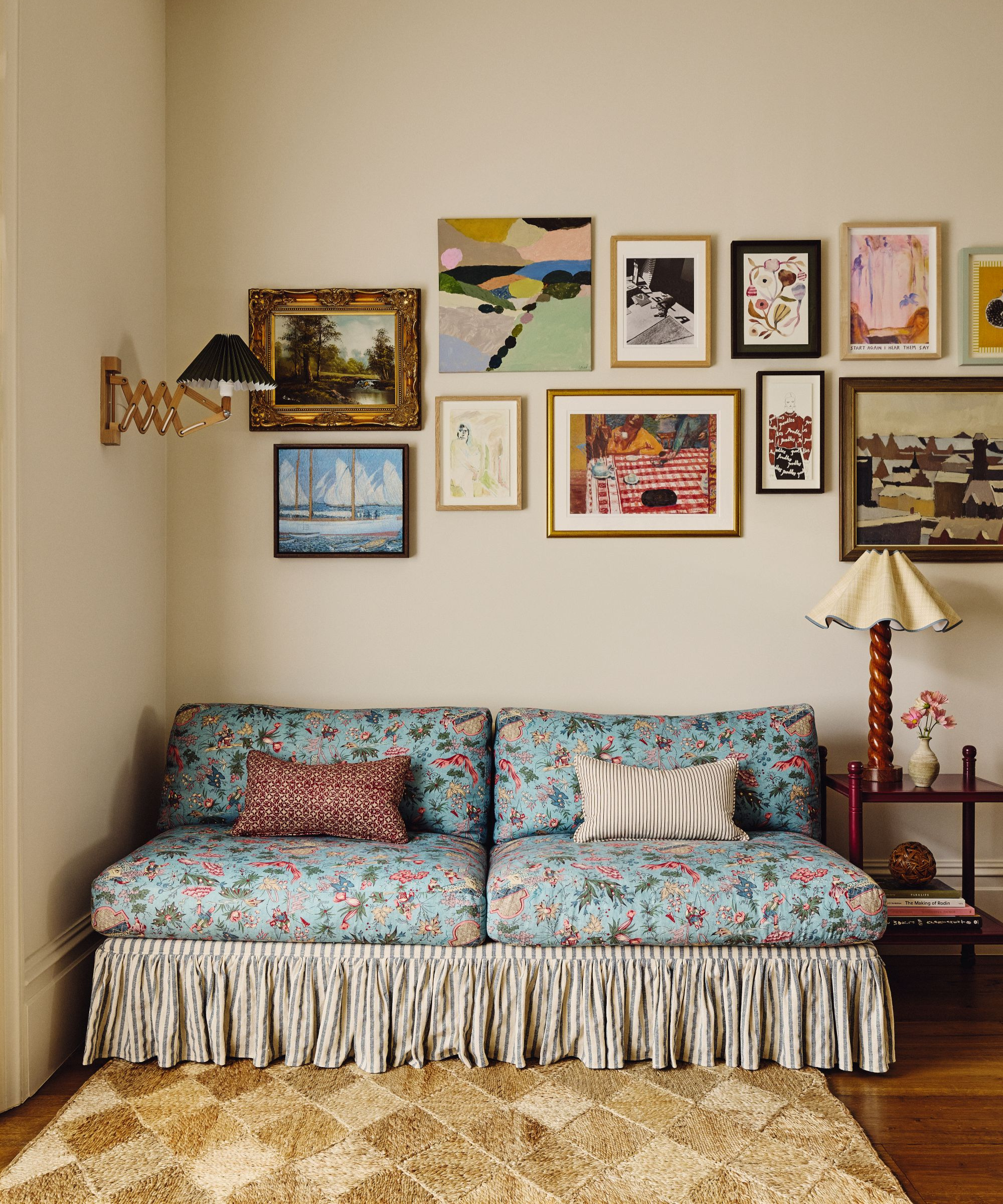a sitting area with a floral printed couch, a jute rug, lots of art on the walls, and a small table with a lamp on the side
