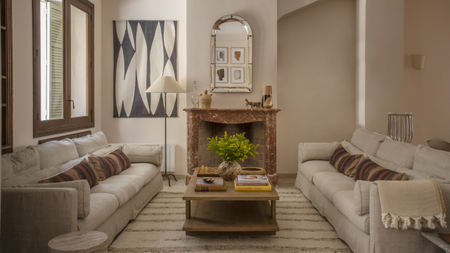 A living room with sofas on either side of the room and a coffee table placed in the middle. There is also a fireplace in the living room with a mirror above it.