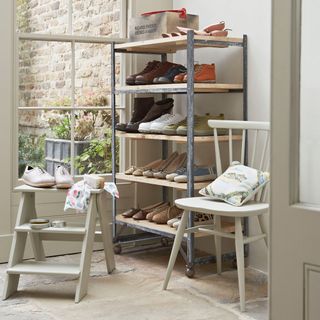 room with wooden rack containing shoes white folding ladder and white chair