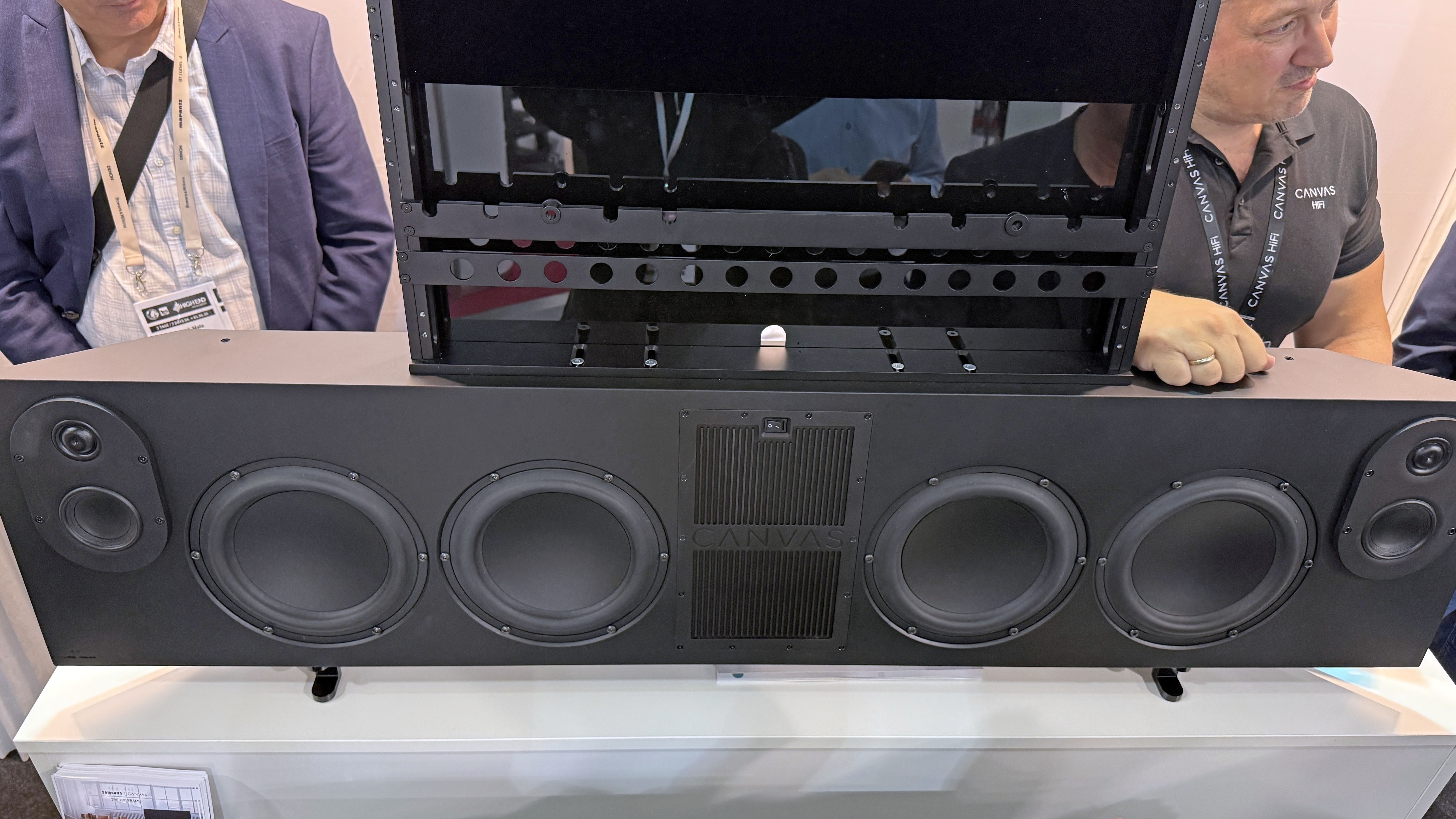 The Canvas L soundbar on a stand at a convention. You can see the speaker arrangement and the size of the TV mount bracket