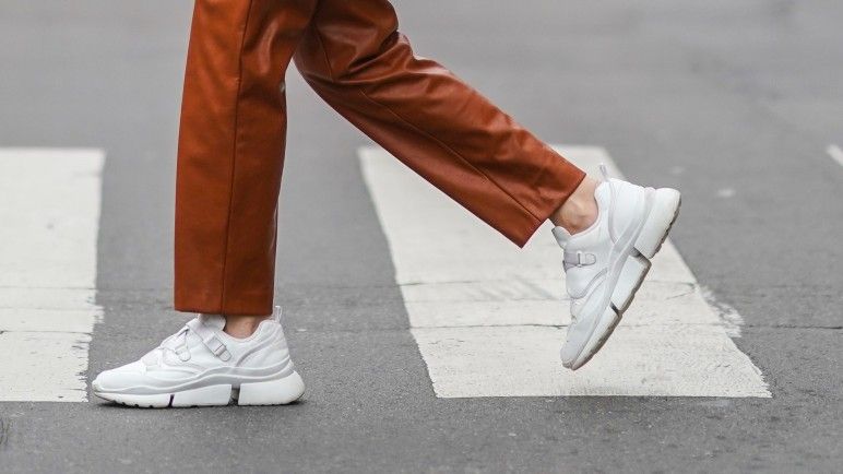 Olesya Senchenko wears earrings, a necklace, a white t-shirt, a black oversized blazer jacket from Lanvin, a brown leather crocodile pattern YSL Saint-Laurent bag, brown leather pants from Antik Batik, white sneakers shoes from Chloe, on February 22, 2021 in Paris, France.