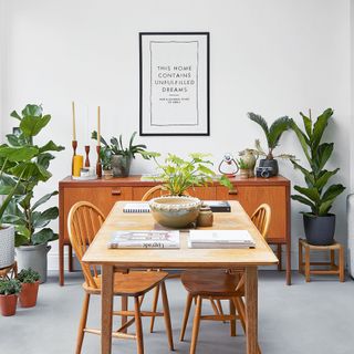 white dining room with wooden table and chairs and houseplants with quote print on wall