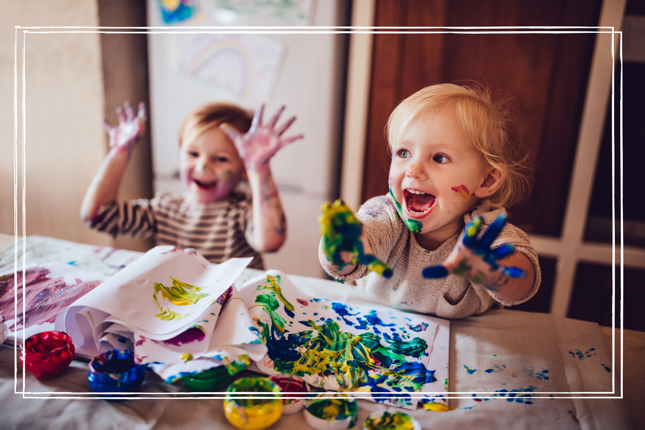 Two young children with paint all over their hands and faces are laughing