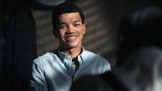 Justice Smith smiles uncomfortably while talking in Ken Watanabe's office in Pokémon Detective Pikachu.