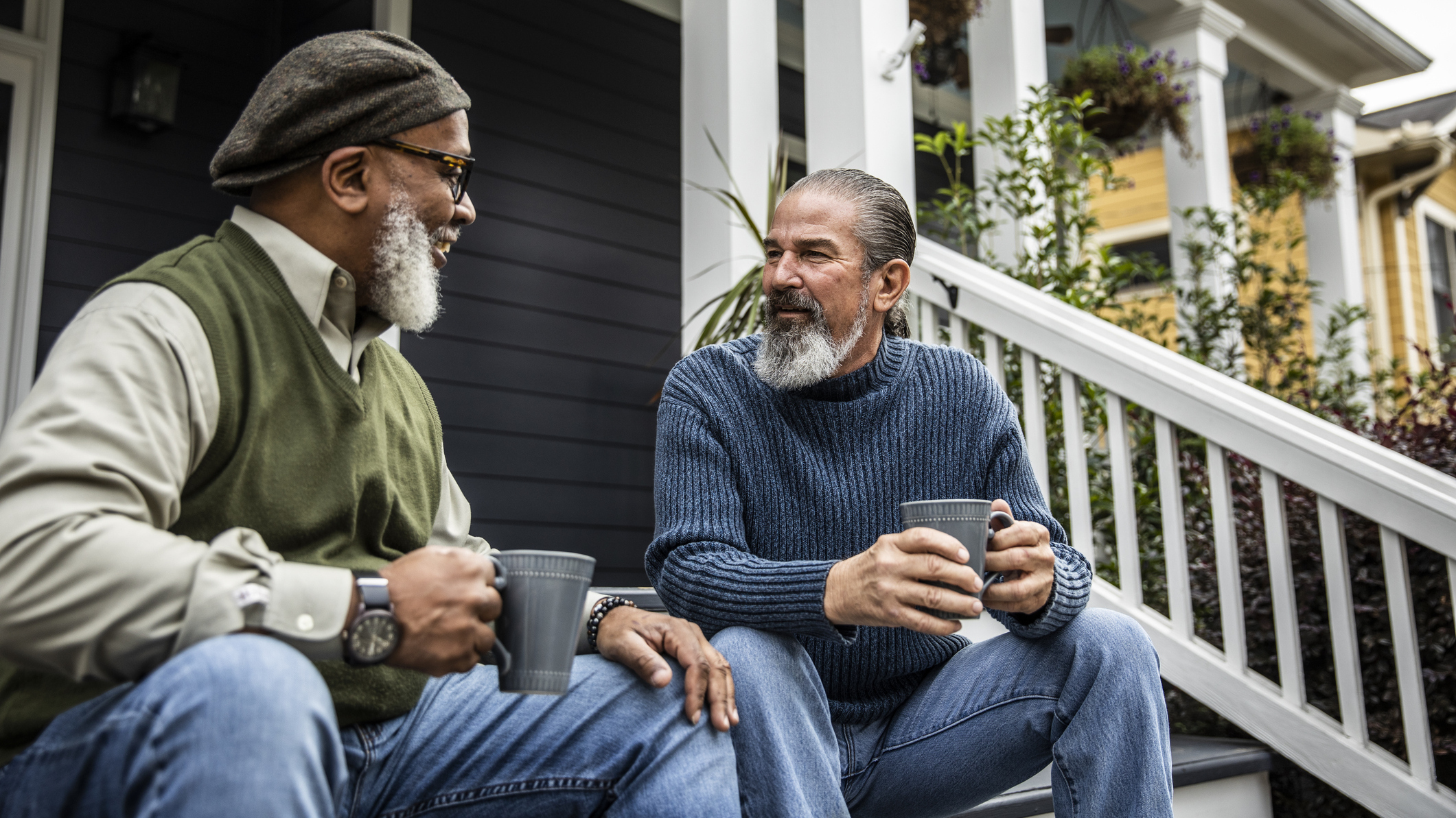 Two men sitting on a front porch talking and holding mugs