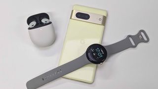 Google Pixel 7 on a table lying next to the Pixel Buds Pro and with a Pixel Watch on top of it