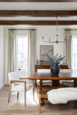 dining space with ceiling beams white upholstered chair and wooden bench seat with sheepskin and wooden rectangular table with wood flooring