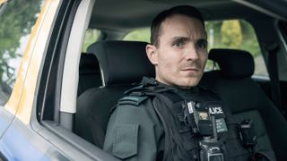 Stevie Neil (Martin McCann) in uniform in a police car in Blue Lights