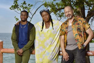 Karlus Brice (Stephen Odubola), Paulette Brice (Michelle Greenidge) and Damon Clarke (Mark Holden) stand on a veranda, with their backs to the ocean. Paulette has her arms around their shoulders, and they are all frowning.