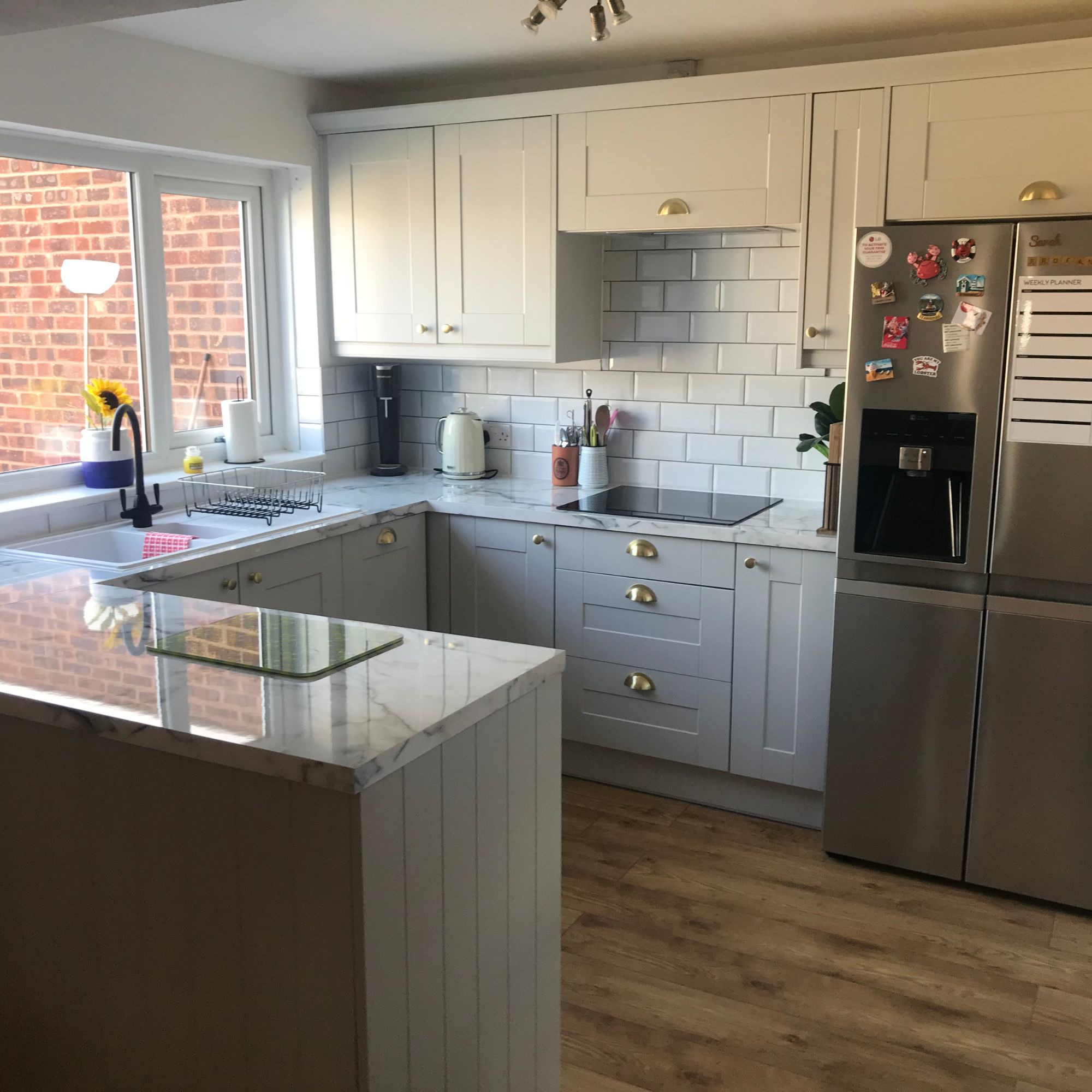 Kitchen with light grey cupboards, marble look worktops, white metro tiles, a peninsula and American-style fridge freezer