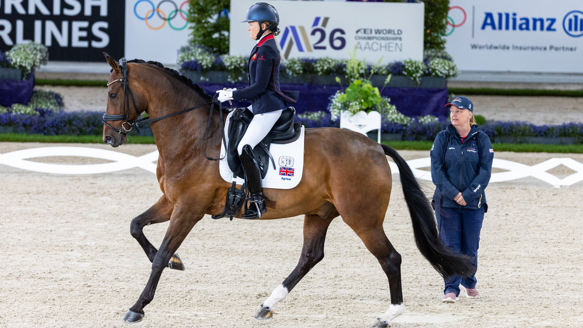 Nicola Naylor rides her horse Humberto L down the centre line at the World Para Dressage Championships in Aachen, while just to one side of her, her caller Julie Riches stands unmounted beside her