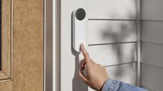A hand press the button on the Nest Doorbell mounted on a door frame