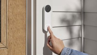 A hand pressing the button on the Nest Doorbell mounted on a door frame