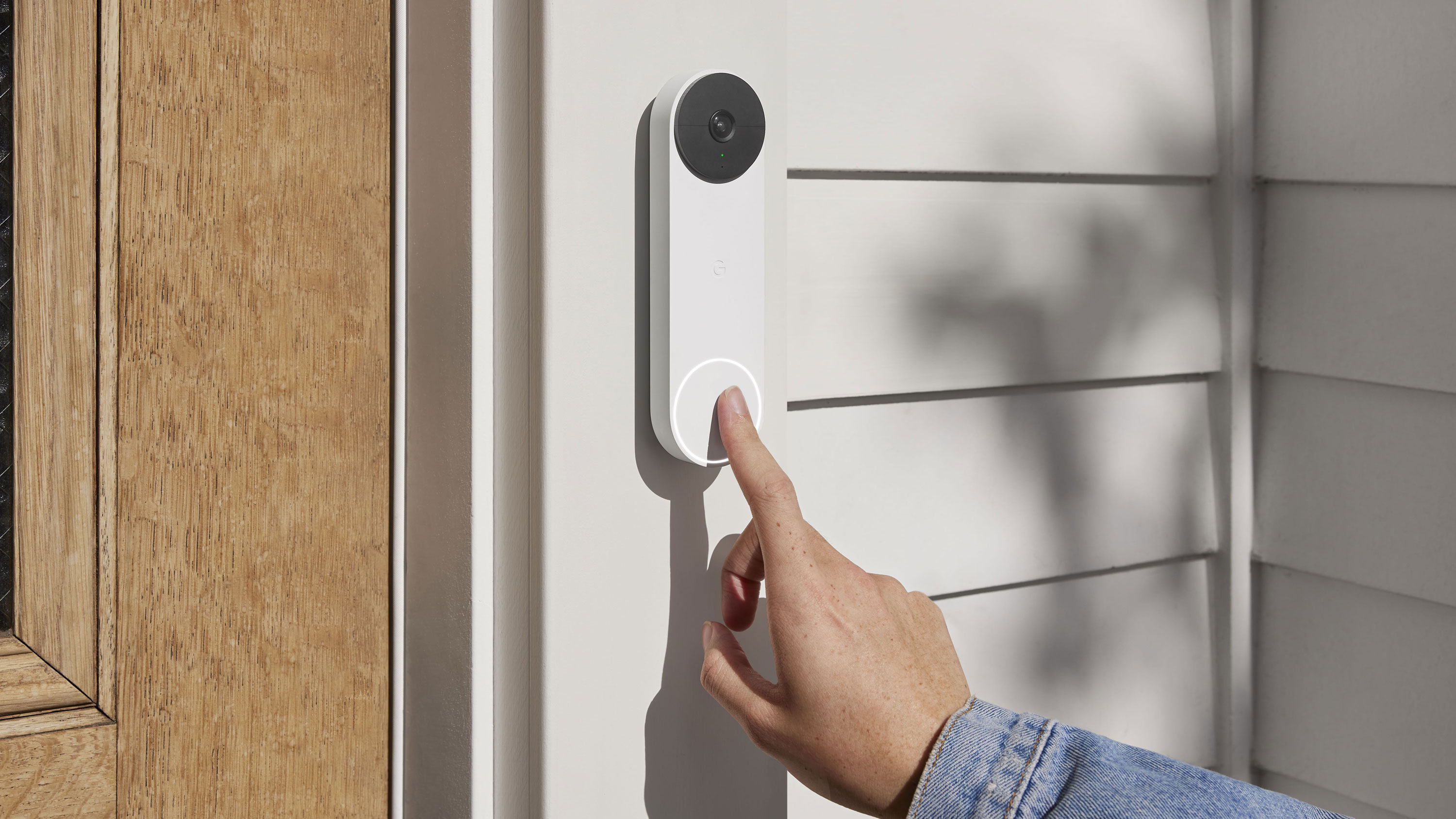 A hand press the button on the Nest Doorbell mounted on a door frame