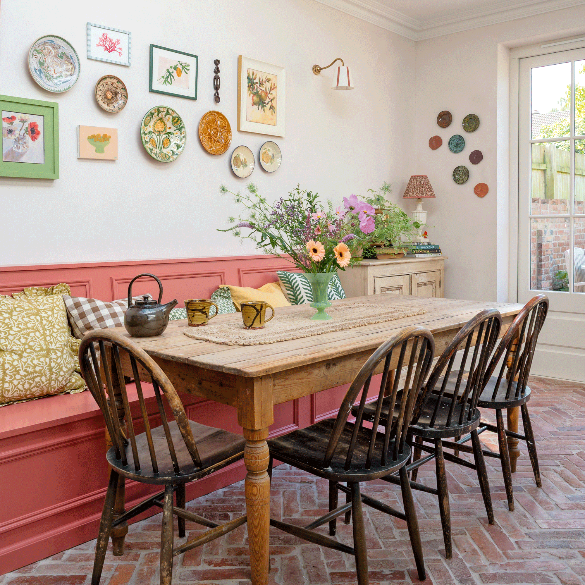 a dining area in a kitchen with pink banquette seating and a rustic dining table with dark wood  chairs