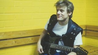 Bryan Adams sits against a yellow wall, backstage with a Charvel Superstrat