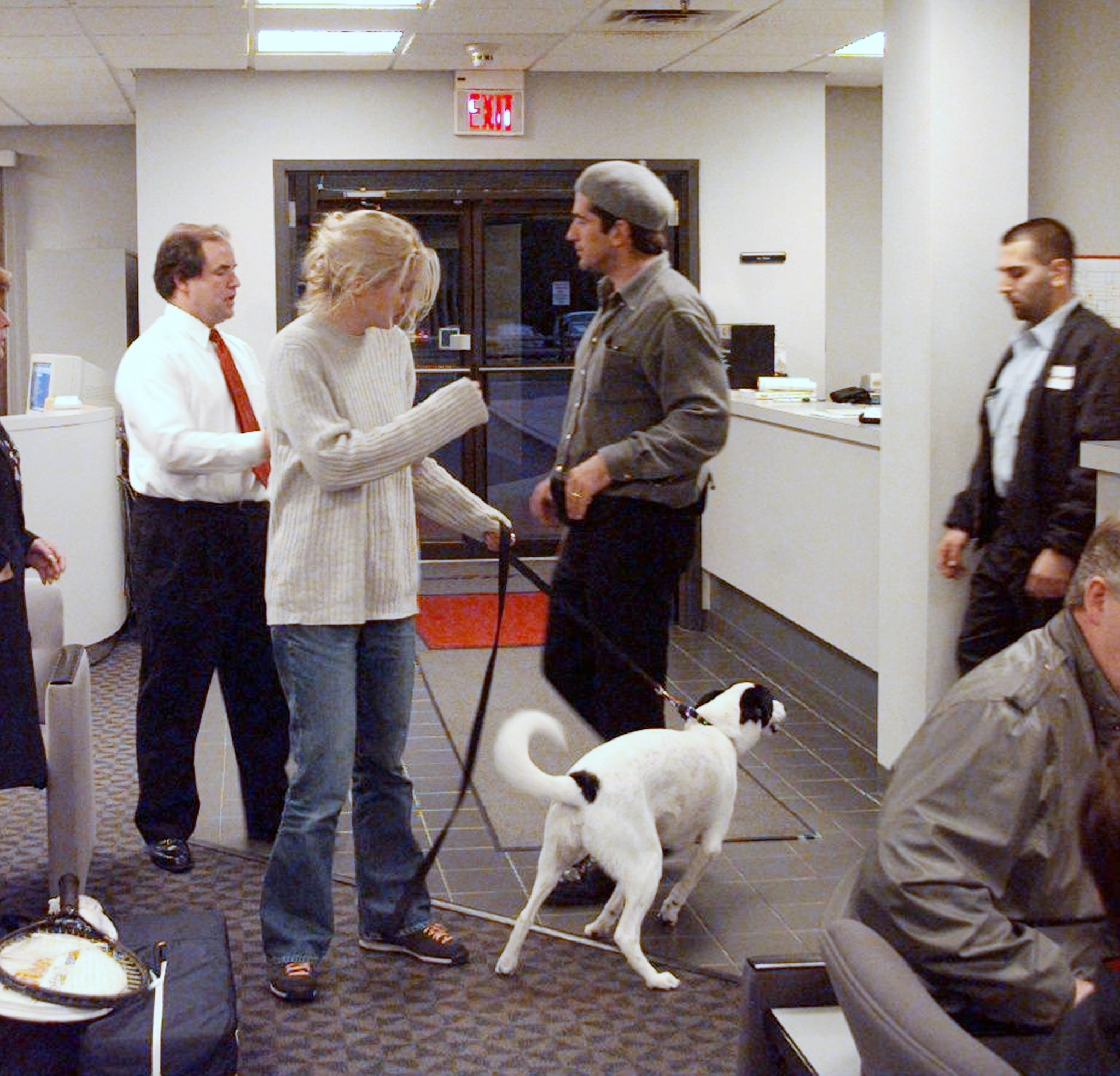 Carolyn Bessette-Kennedy wears a cream rollneck sweater and jeans and holds her dog on a lead, standing next to husband John F. Kennedy Jr who wears a black beret at Teterboro Airport