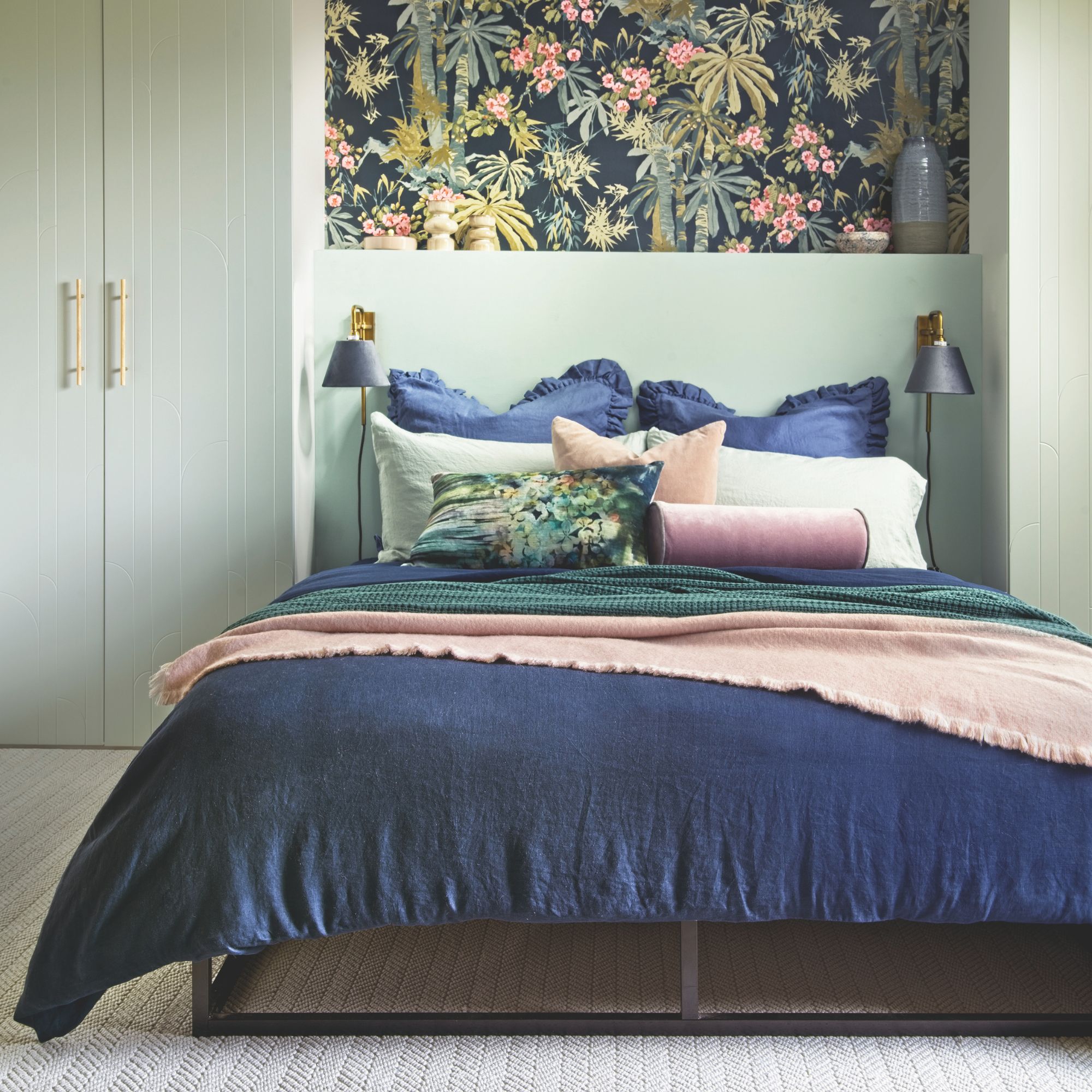 Green painted bedroom with blue and pink bedding and fitted wardrobes either side of the bed