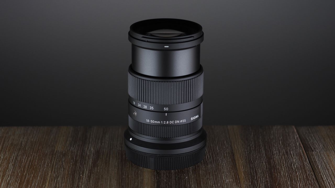 The Sigma 18-50mm f/2.8 DC DN | C Canon RF lens on a wooden surface against a dark background with moody lighting