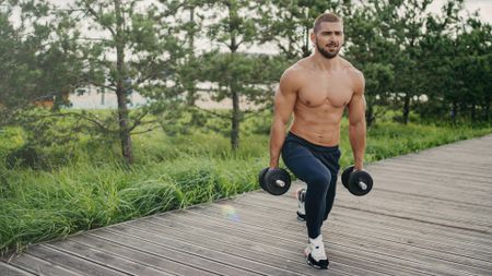 Man outdoors performing lunge with set of dumbbells on a walkway in nature