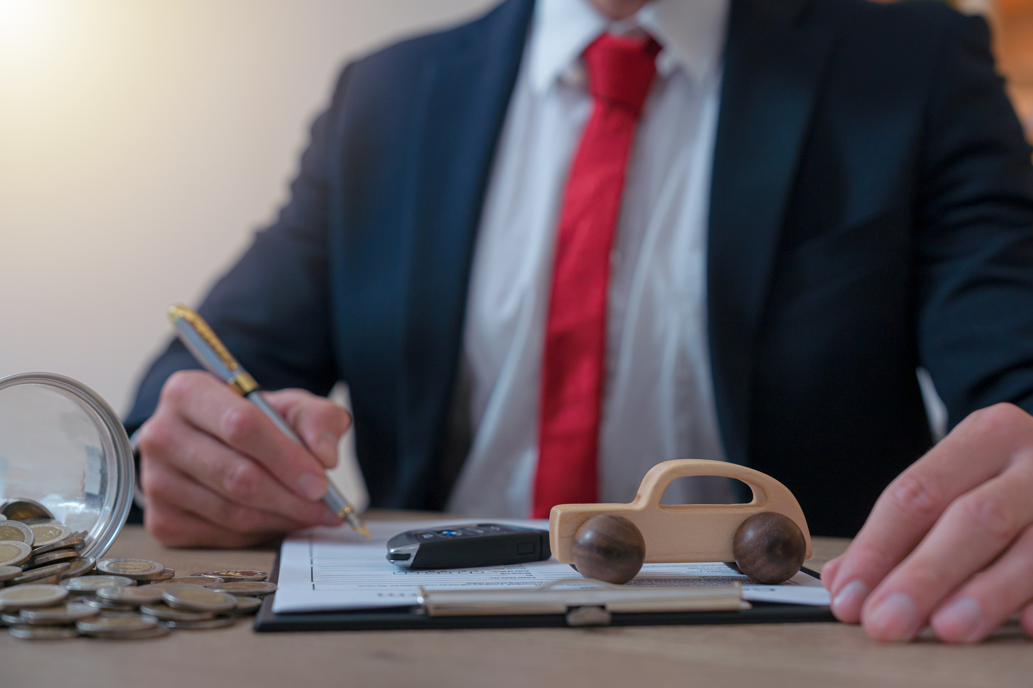 Man sitting in front of a toy car with money and paperwork on his desk representing motor finance