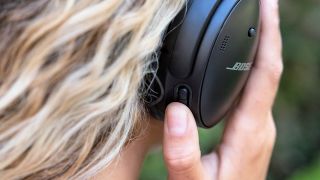 Listing image for best noise-cancelling headphones showing Bose QuietComfort 45 showing female with blond hair wearing headphones and placing hand on right earcup